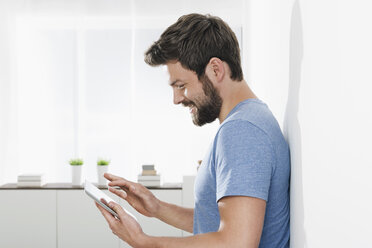 Portrait of young man leaning against wall using mini tablet - PDF000649