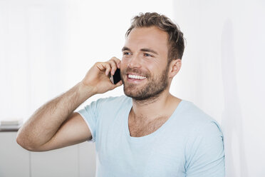 Portrait of young man leaning against wall telephoning with smartphone - PDF000645