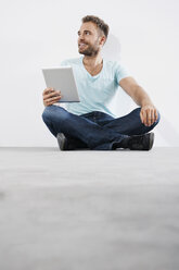 Porträt eines jungen Mannes, der auf dem Boden sitzt und einen Tablet-Computer hält - PDF000648