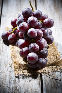 Rote Weintrauben auf Jute und Holztisch - MAEF007859