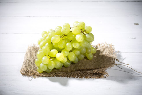 Kernlose weiße Weintrauben auf Jute und weißem Holztisch - MAEF007865
