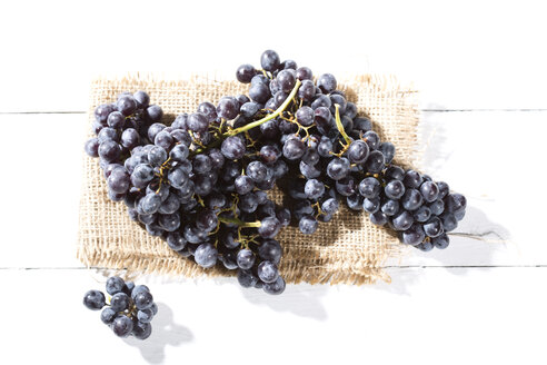 Kernlose blaue Weintrauben auf Jute und weißem Holztisch - MAEF007867