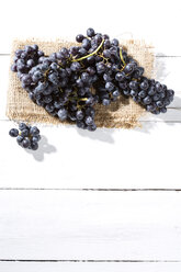 Kernlose blaue Weintrauben auf Jute und weißem Holztisch - MAEF007868