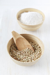 Bowl of buckwheat grains with wooden shovel and bowl of buckwheat flour on white wooden table - EVGF000432