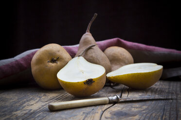 Sliced and whole pears (Pyrus), a knife and a kitchen towel on wooden table - LVF000646