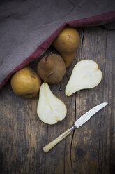 Sliced and whole pears (Pyrus), a knife and a kitchen towel on wooden table - LVF000645