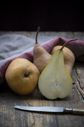 Sliced and whole pears (Pyrus), a knife and a kitchen towel on wooden table - LVF000644
