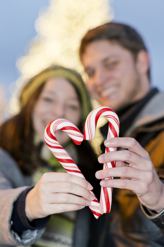 Deutschland, Berlin, junges Paar hält Zuckerstangen in Form eines Herzens, lizenzfreies Stockfoto