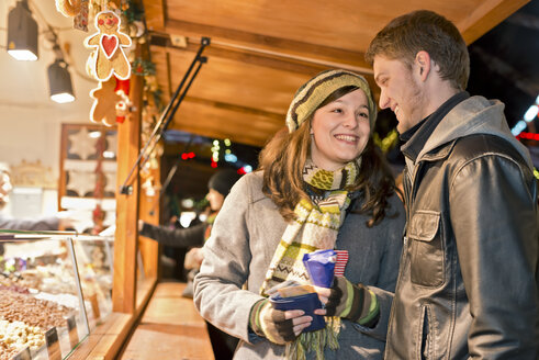 Deutschland, Berlin, junges Paar kauft gebrannte Mandeln auf dem Weihnachtsmarkt - CLPF000062