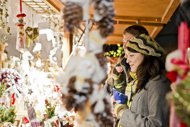 Germany, Berlin, young couple watching offerings at Christmas market - CLPF000060