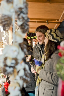 Deutschland, Berlin, junges Paar betrachtet Angebote auf dem Weihnachtsmarkt - CLPF000059