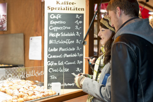 Deutschland, Berlin, junges Paar kauft frittiertes Gebäck auf dem Weihnachtsmarkt - CLPF000057