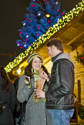 Germany, Berlin, young couple with deep-fried pastries at Christmas market - CLPF000056