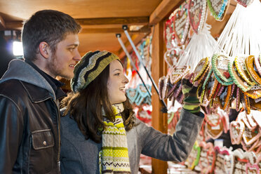 Germany, Berlin, young couple watching offerings at Christmas market - CLPF000055