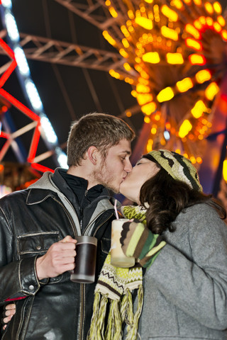 Deutschland, Berlin, glückliches junges Paar küsst sich auf dem Weihnachtsmarkt vor einem beleuchteten Riesenrad, lizenzfreies Stockfoto
