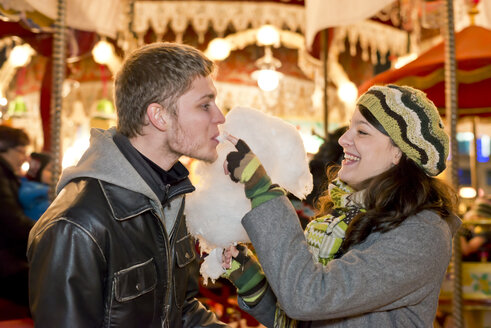 Deutschland, Berlin, glückliches junges Paar mit Zuckerwatte auf dem Weihnachtsmarkt - CLPF000050