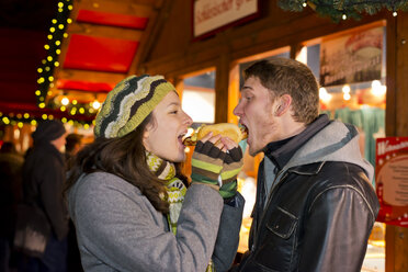 Germany, Berlin, young couple eating grill sausage at Christmas market - CLPF000048