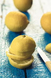 Ganze und geschnittene Zitronen und Küchenmesser auf blauem Holztisch - SARF000248