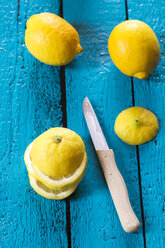 Ganze und geschnittene Zitronen und Küchenmesser auf blauem Holztisch - SARF000250