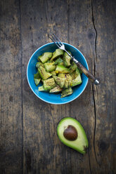 Bowl of avocado salad (Persea americana) and half of avocado on wooden table - LVF000661
