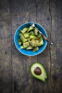 Schüssel mit Avocadosalat (Persea americana) und halbe Avocado auf Holztisch - LVF000661