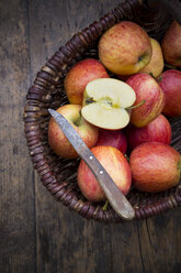 Korb mit geschnittenen und ganzen roten Äpfeln und Küchenmesser auf Holztisch - LVF000683
