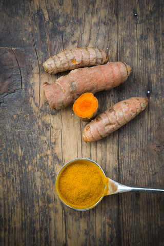 Spoon of curcuma powder and curcuma roots (Curcuma longa) on wooden table, view from above stock photo