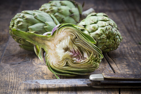 Sliced and whole organic artichokes and kitchen knife on wooden table - LVF000675