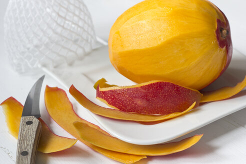 Mango (Mangifera indica), Schale und Messer auf weißem Teller - YFF000037