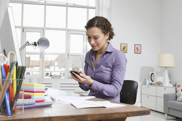 Frau zu Hause am Schreibtisch mit Computer und Telefon - RBYF000467