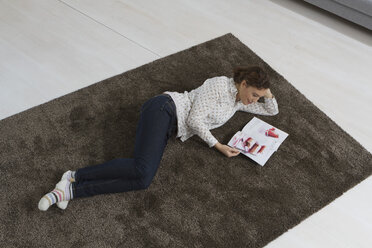 Woman lying on carpet reading magazine - RBYF000348