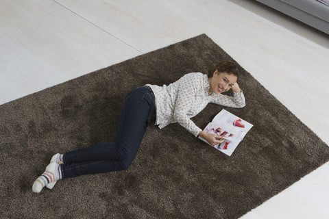 Frau liegt auf Teppich und liest Zeitschrift, lizenzfreies Stockfoto