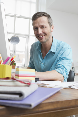 Porträt eines lächelnden Mannes am Schreibtisch, lizenzfreies Stockfoto