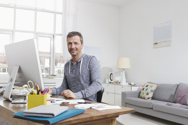 Mann zu Hause sitzt am Schreibtisch mit Computer - RBYF000365