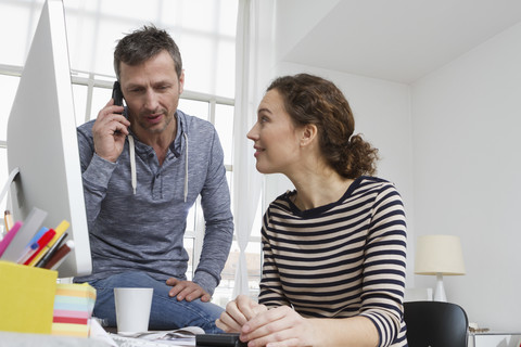 Mann und Frau an einem Schreibtisch mit Computer und Telefon, lizenzfreies Stockfoto