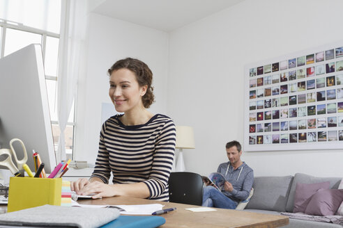 Woman at home sitting at desk with computer and man in background - RBYF000370