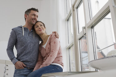 Lächelndes Paar, das sich am Fenster umarmt - RBYF000378