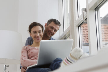 Couple sitting on windowsill using laptop - RBYF000380