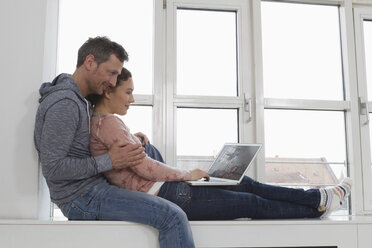 Couple sitting on windowsill using laptop - RBYF000477