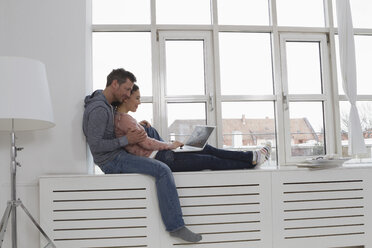 Paar sitzt auf der Fensterbank und benutzt einen Laptop - RBYF000478