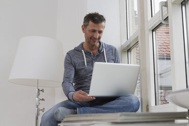 Mann sitzt auf der Fensterbank und benutzt einen Laptop - RBYF000387