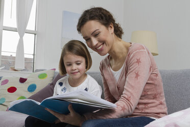 Mother and daughter on couch with book - RBYF000409