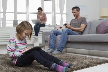 Mother, father and daughter using portable devices in living room - RBYF000483