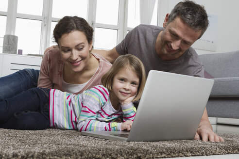 Vater, Mutter und Tochter benutzen Laptop auf Teppich im Wohnzimmer - RBYF000465