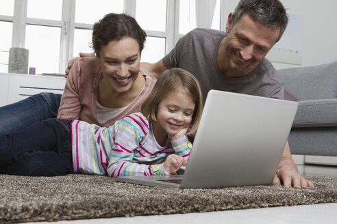 Vater, Mutter und Tochter benutzen Laptop auf Teppich im Wohnzimmer - RBYF000464