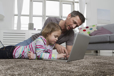 Father and daughter using laptop on carpet in living room - RBYF000485