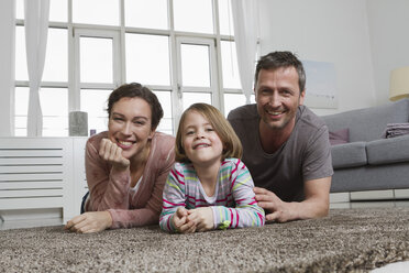 Happy mother, father and daughter lying on carpet in living room - RBYF000492