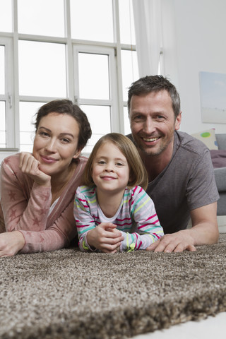 Glückliche Mutter, Vater und Tochter liegen auf dem Teppich im Wohnzimmer, lizenzfreies Stockfoto