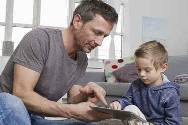 Vater und Sohn benutzen einen Tablet-Computer im Wohnzimmer - RBYF000494