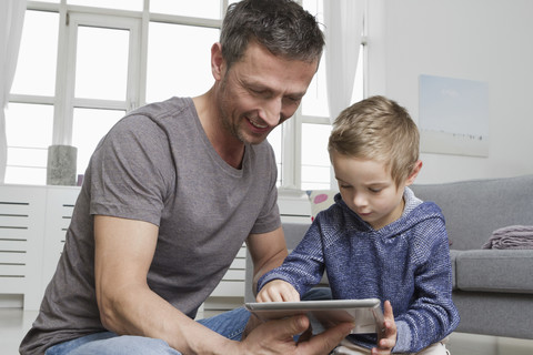 Vater und Sohn benutzen einen Tablet-Computer im Wohnzimmer, lizenzfreies Stockfoto